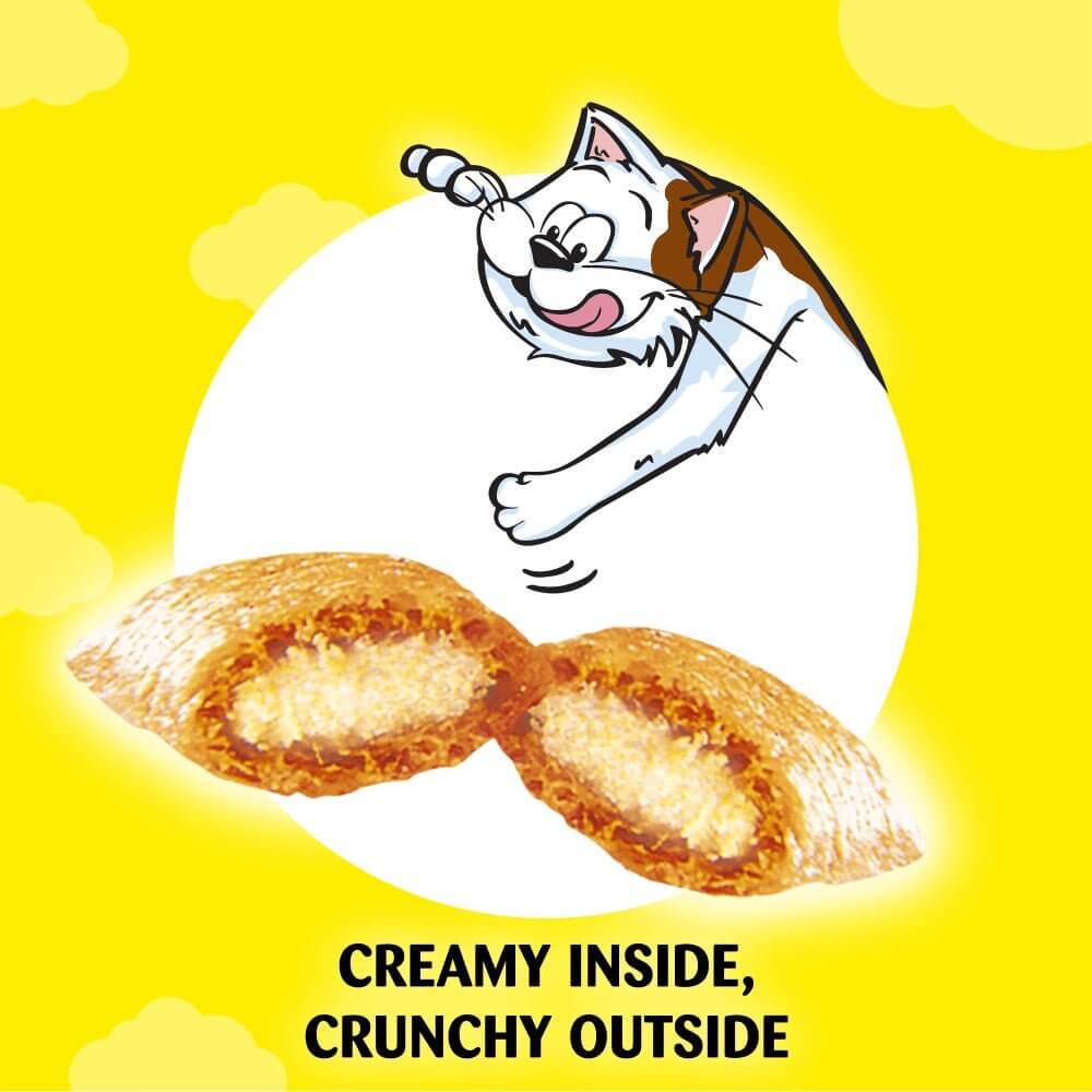 Cat excitedly reaching for Dreamies Cat Treats with a creamy inside and crunchy outside, against a bright yellow background.