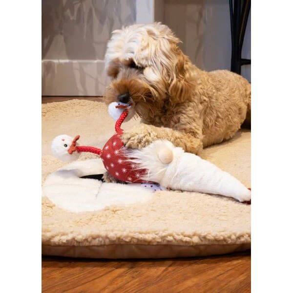 Dog playing with Greg Gonk festive toy featuring a squeaker and rope legs on a cozy pet bed.