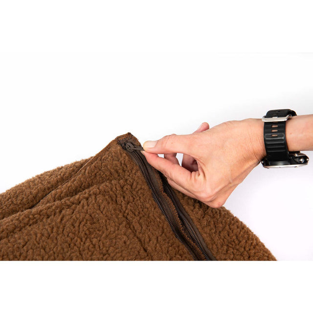 Close-up of a hand unzipping the soft, brown material of a cozy dog bed.