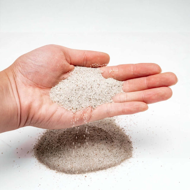 Hand holding UNS Controsand natural substrate for aquariums, showcasing its fine granule texture.