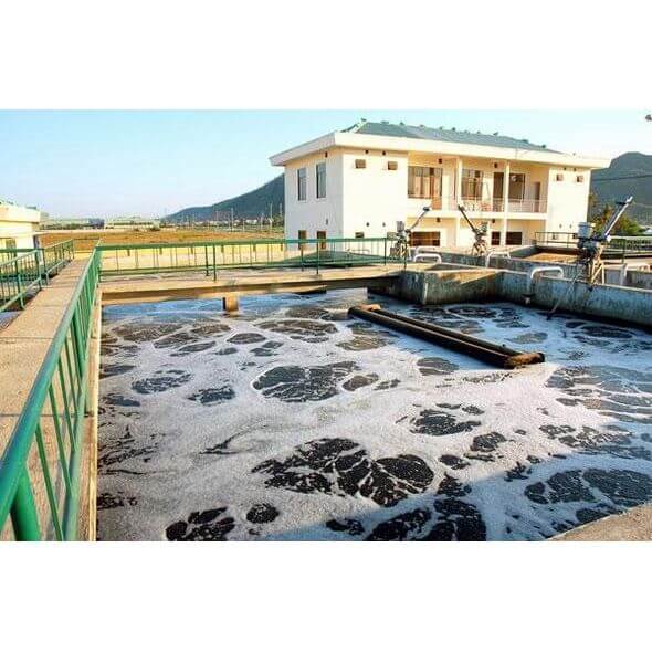 Industrial wastewater treatment facility with microbial activity and foam on surface.