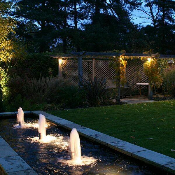 illuminated garden fountain with multiple jets and lush greenery at dusk