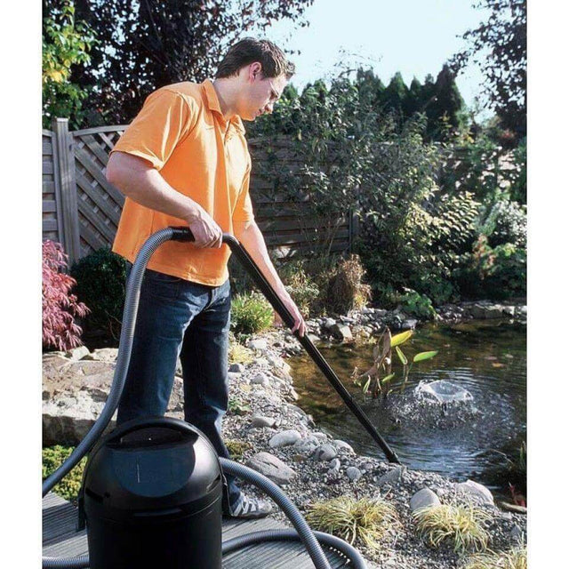 Man using Pontec Pondomatic Pond and Pool Vacuum Cleaner near a garden pond, demonstrating effective sludge removal.