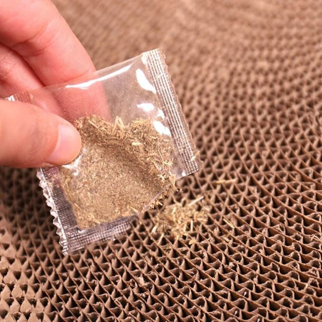 Hand holding a pack of catnip above a round cardboard cat scratcher surface.