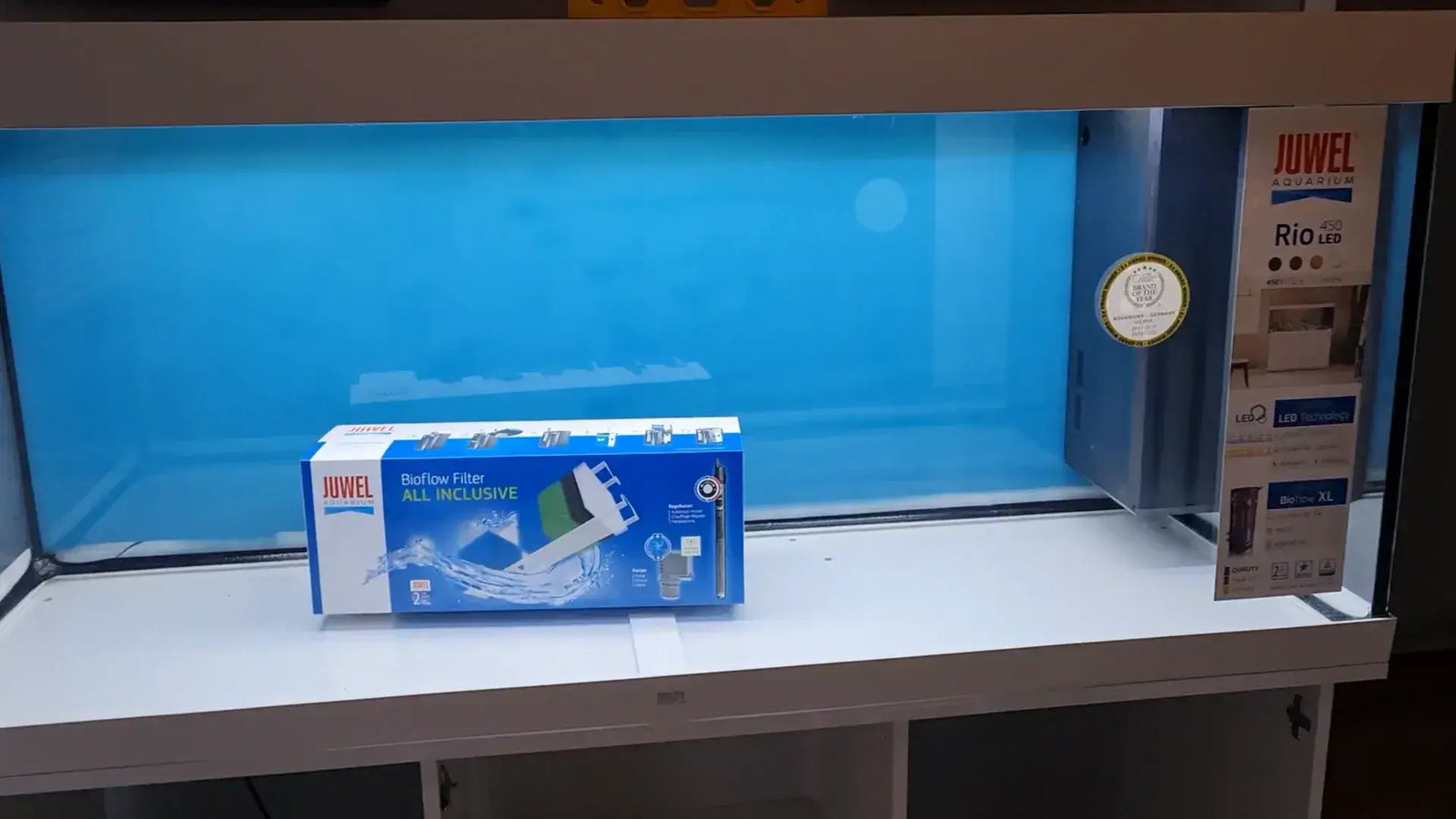 Juwel Aquarium Rio 450 setup featuring the aquarium, filter, and documentation in a bright blue backdrop.