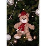 Soft teddy bear with a festive hat and scarf hanging on a Christmas tree, adding holiday charm and cuddly fun.