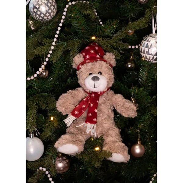 Soft teddy bear with a festive hat and scarf hanging on a Christmas tree, adding holiday charm and cuddly fun.