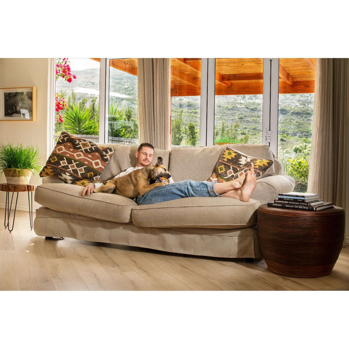 Man relaxing on a couch with a dog, showcasing a cozy living room with natural light.