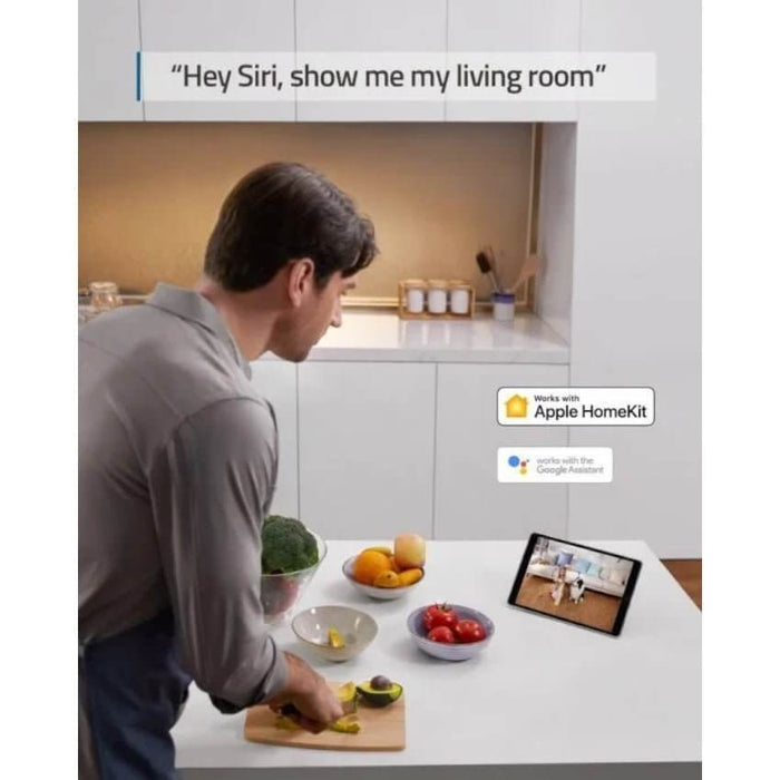 man talking to smart device while cooking in modern kitchen with fresh ingredients and smart screen displaying a room view.