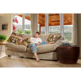 Man sitting on a couch with a dog, enjoying a cozy moment indoors with large windows and decorative pillows.