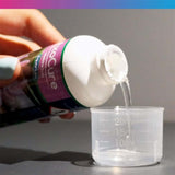 Pouring NT Labs AxoCure medicine from a bottle into a measuring cup for axolotl treatment.