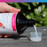 Hand pouring NT Labs Koi Care Argusol liquid into a measuring cup outdoors.