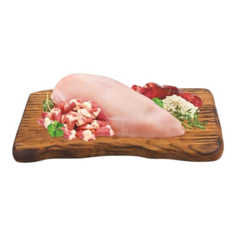 Sliced chicken breast on a wooden board with various cuts of meat and herbs for a delicious meal preparation.