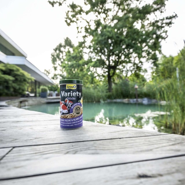 Tetra Pond Variety Sticks canister by a serene pond, providing essential nutrients for healthy pond fish growth.