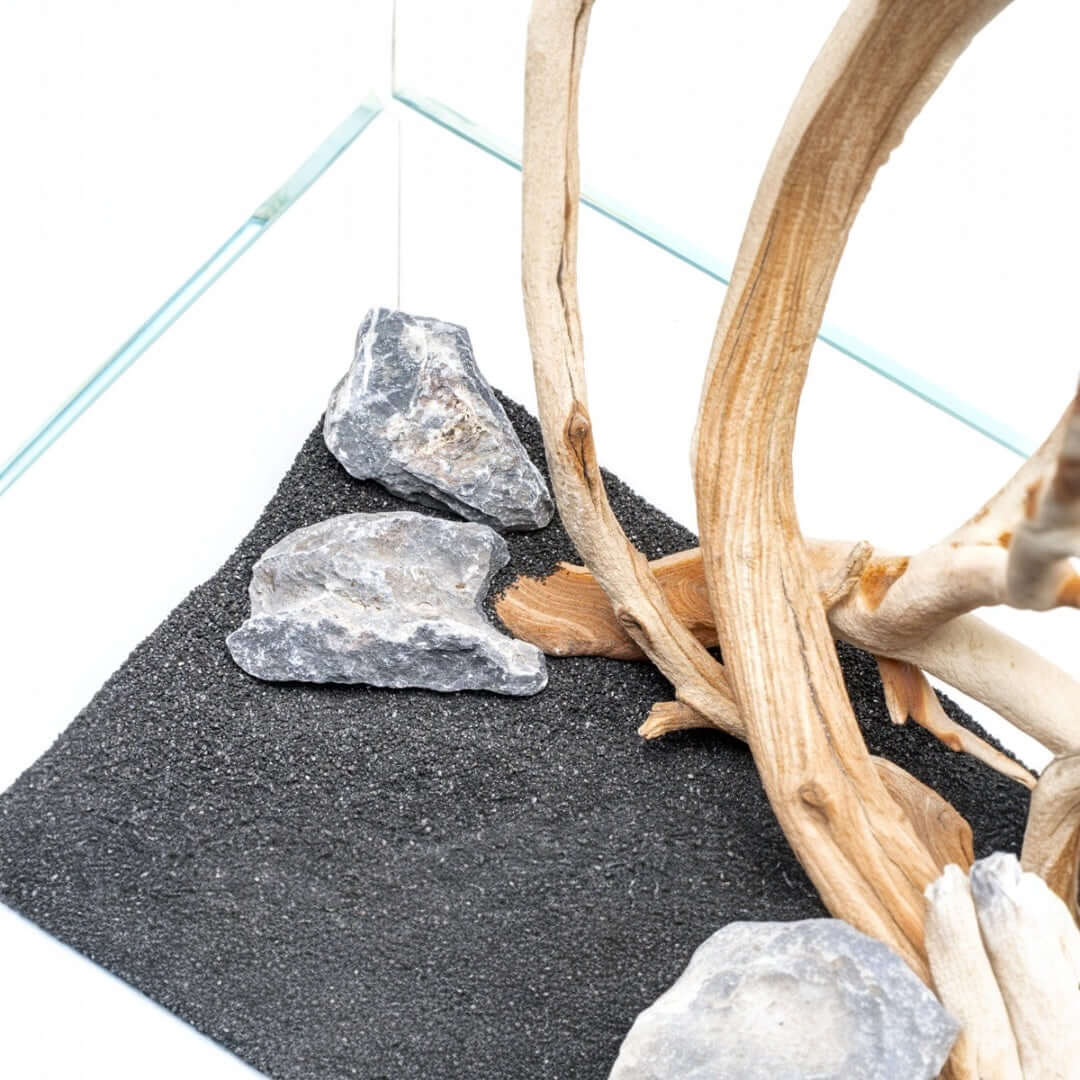 Natural aquarium substrate with black sand, stones, and driftwood for aquascaping.