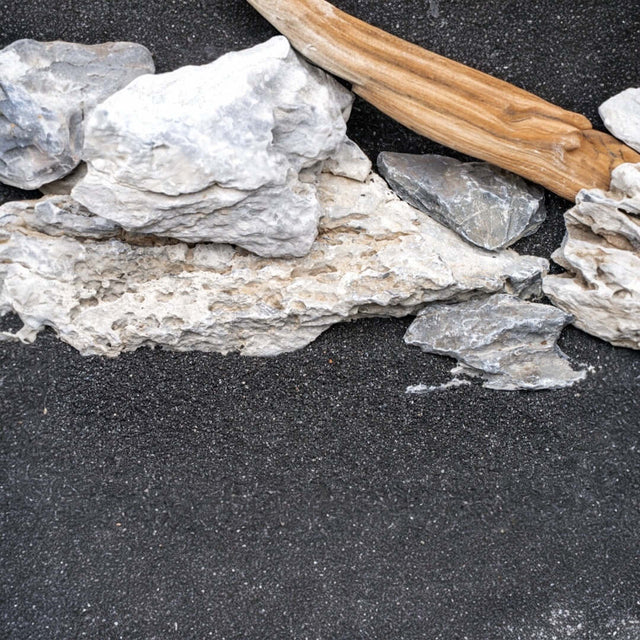 Natural substrate elements for aquascaping, featuring rocks and driftwood over black sand for aquariums.