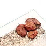 Natural substrate with reddish rocks in a glass aquarium for aquascaping and terrarium use.