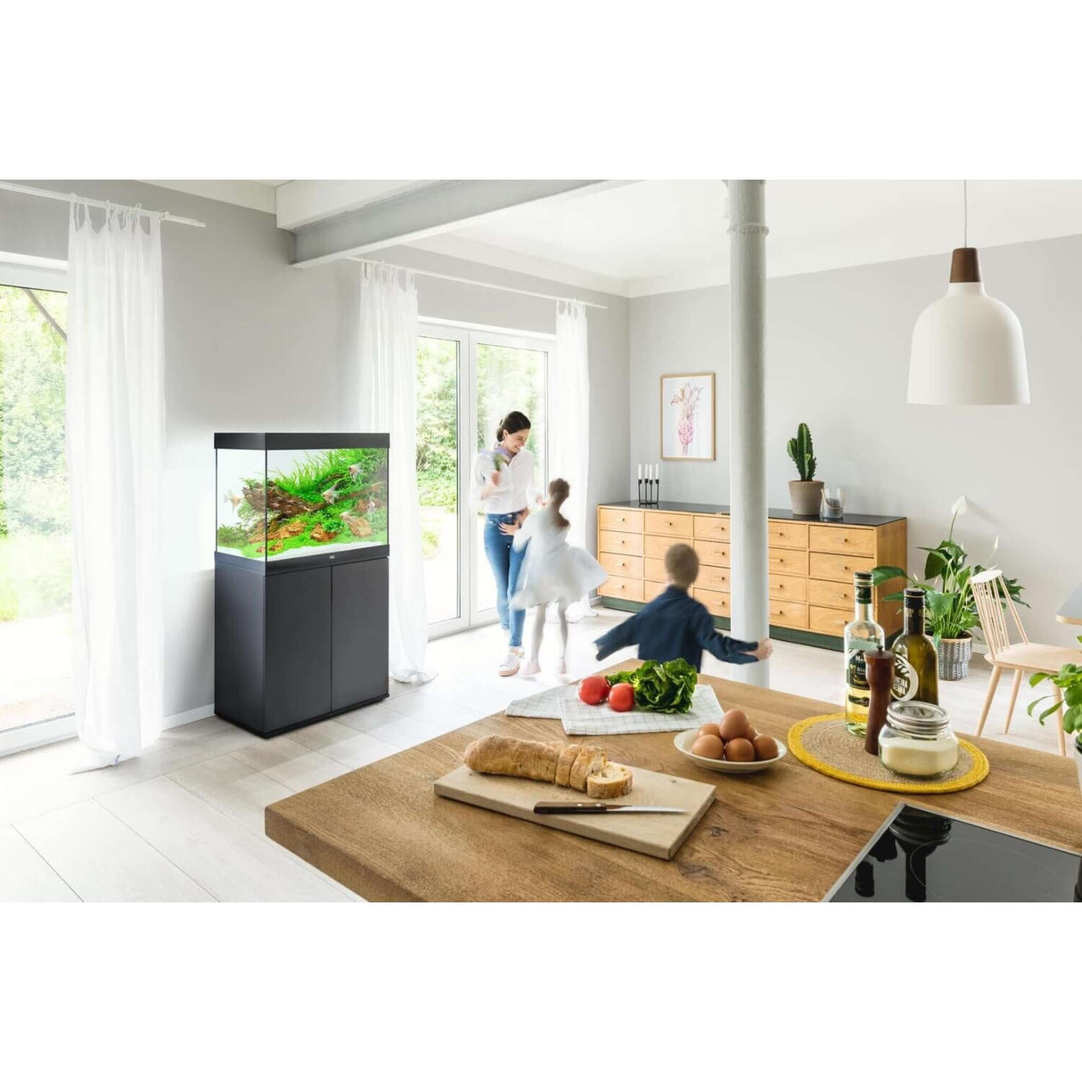 Family enjoying time together in a bright room featuring a Juwel Lido aquarium and cabinet on a stylish wooden table.