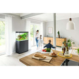 Family enjoying time together in a bright room featuring a Juwel Lido aquarium and cabinet on a stylish wooden table.
