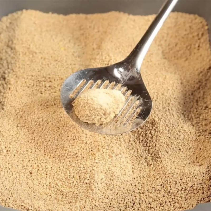 Close-up of clumping cat litter being scooped with a metal scoop, showcasing its natural texture and color.